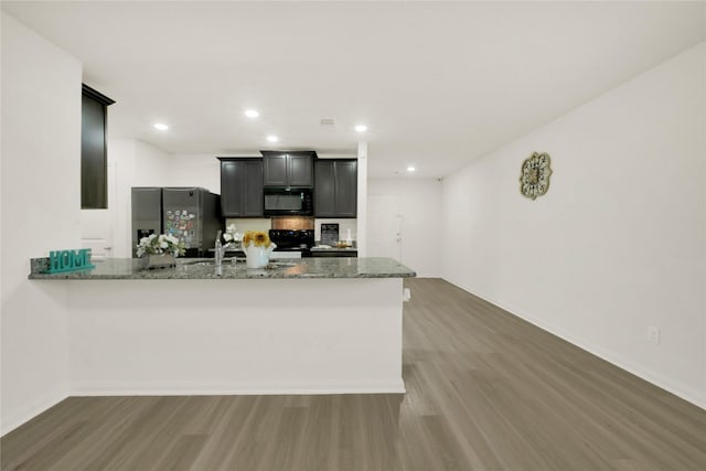 kitchen featuring wood finished floors, a peninsula, recessed lighting, stone countertops, and black appliances