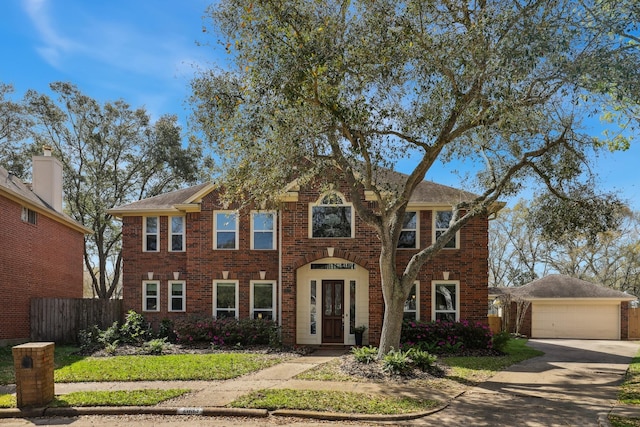 colonial inspired home with an outdoor structure, fence, brick siding, and driveway