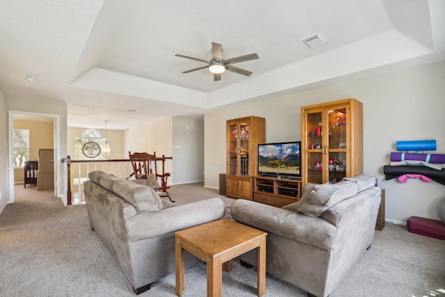 living area featuring baseboards, visible vents, a tray ceiling, ceiling fan, and light carpet