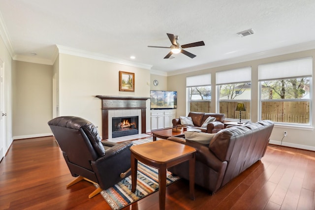 living area with visible vents, baseboards, ceiling fan, a tiled fireplace, and dark wood-style flooring