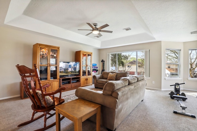 carpeted living room with a raised ceiling, a ceiling fan, visible vents, and baseboards