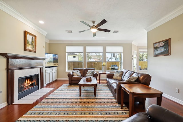 living area with visible vents, dark wood-style flooring, ceiling fan, and a tiled fireplace