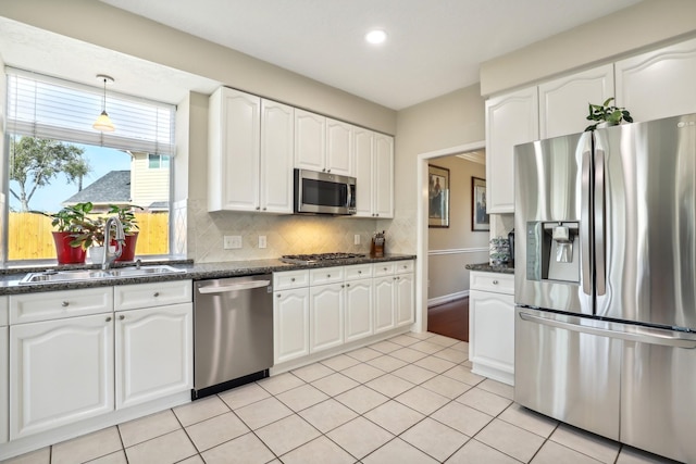 kitchen featuring light tile patterned floors, a sink, stainless steel appliances, white cabinetry, and backsplash