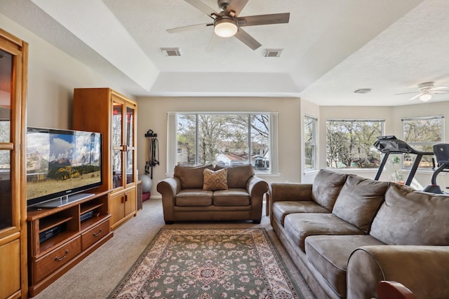 living area with a tray ceiling, visible vents, carpet, and a ceiling fan