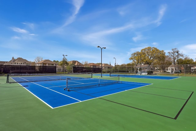 view of tennis court with community basketball court, fence, and a residential view