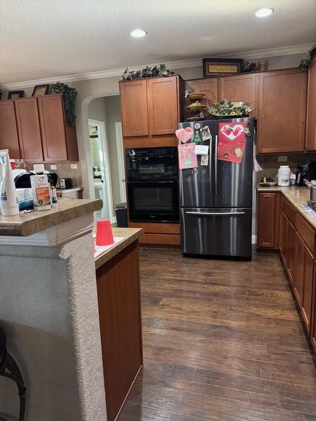 kitchen featuring dark wood-style floors, arched walkways, freestanding refrigerator, dobule oven black, and crown molding