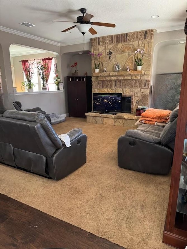 living area featuring visible vents, crown molding, ceiling fan, a fireplace, and arched walkways