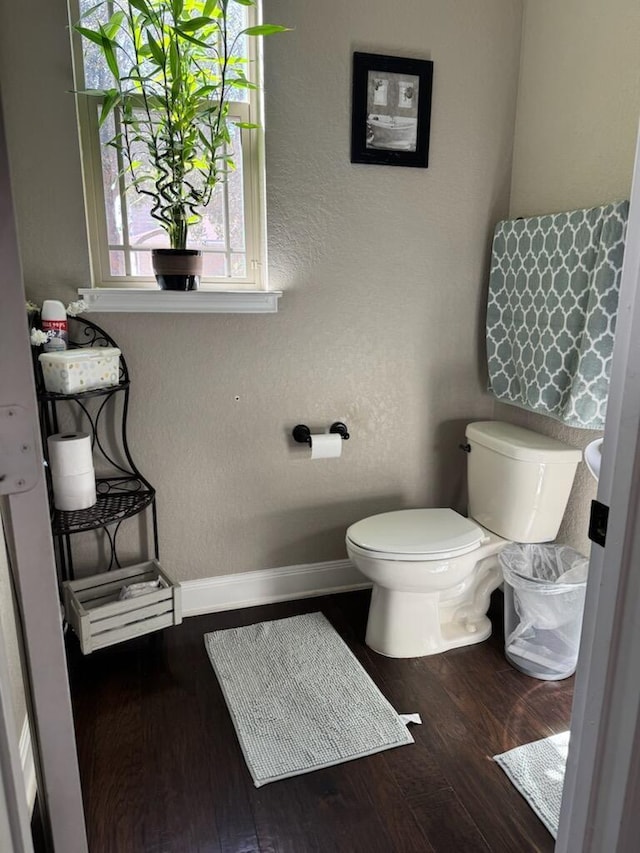 bathroom with toilet, wood finished floors, baseboards, and a textured wall