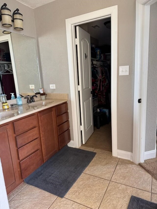 full bathroom featuring tile patterned floors, a walk in closet, baseboards, and vanity