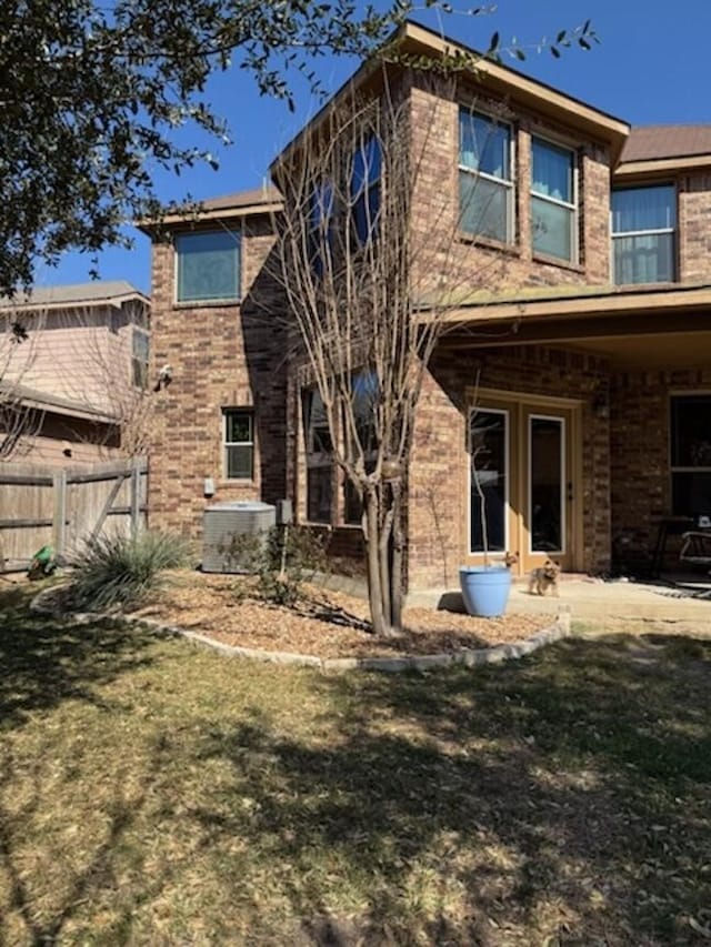 rear view of house with brick siding, cooling unit, a yard, and fence