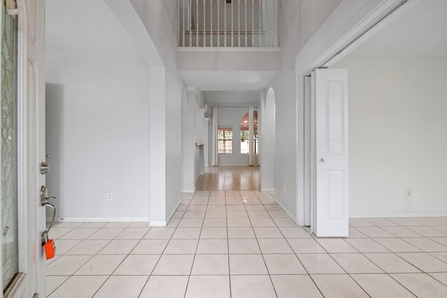 foyer featuring baseboards, arched walkways, a towering ceiling, and light tile patterned flooring