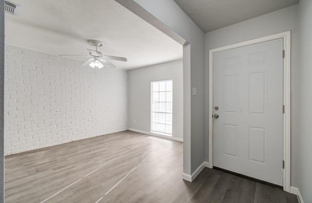 entryway with a ceiling fan, wood finished floors, visible vents, brick wall, and a textured ceiling