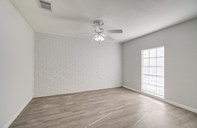 unfurnished room featuring wood finished floors, visible vents, brick wall, ceiling fan, and a textured ceiling