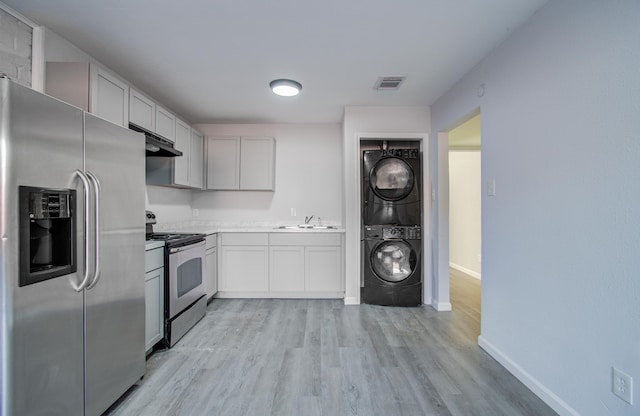 kitchen with visible vents, stacked washing maching and dryer, a sink, under cabinet range hood, and appliances with stainless steel finishes