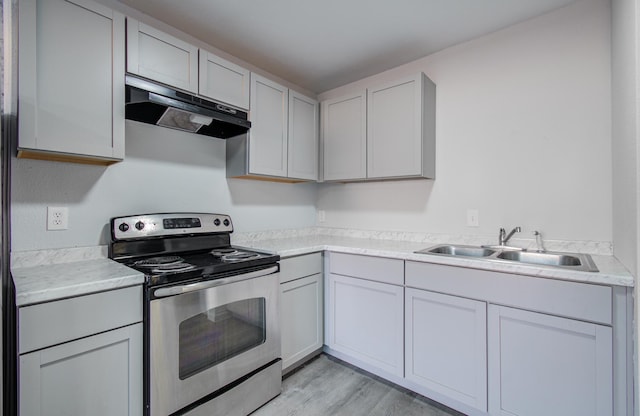 kitchen with electric stove, under cabinet range hood, a sink, light wood-style floors, and light countertops