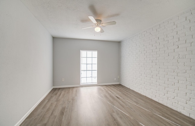 spare room featuring a textured ceiling, wood finished floors, brick wall, baseboards, and ceiling fan