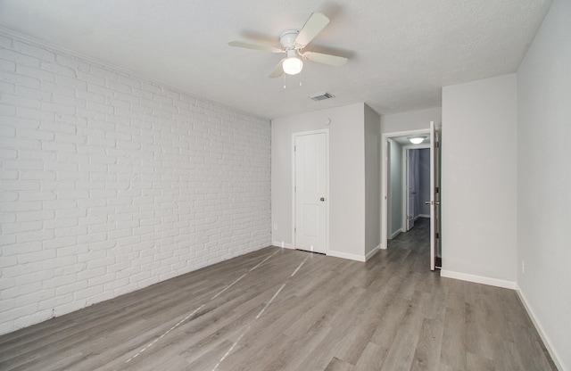 unfurnished bedroom with visible vents, baseboards, wood finished floors, and brick wall