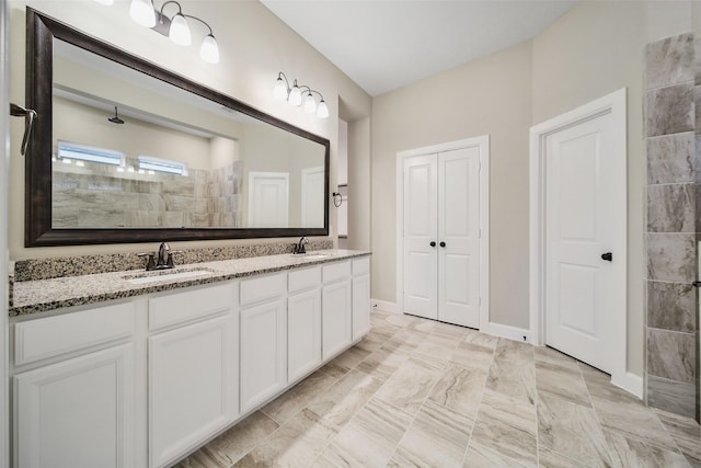 bathroom with double vanity, tiled shower, baseboards, and a sink