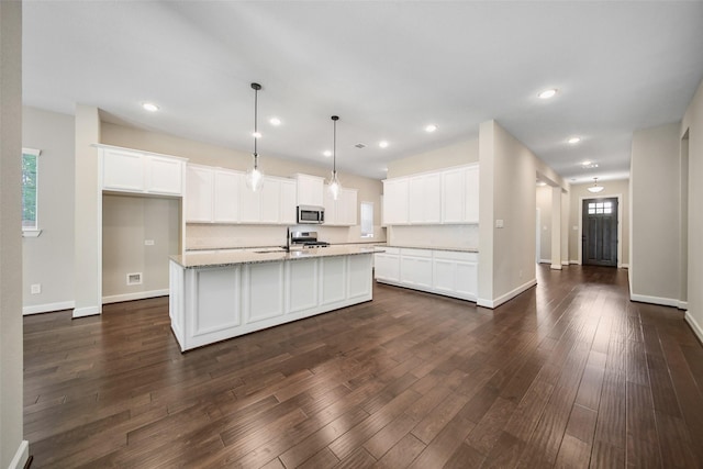 kitchen featuring light stone countertops, dark wood-style floors, an island with sink, white cabinets, and appliances with stainless steel finishes