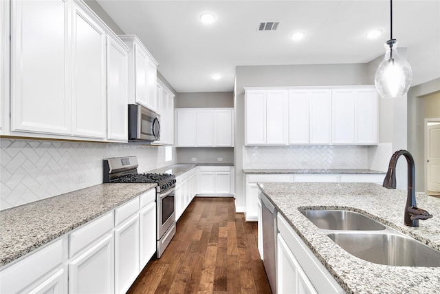 32193 Park Plains Dr, Conroe, TX 77385 - kitchen featuring appliances with stainless steel finishes, a sink, dark wood finished floors, white cabinets, and decorative backsplash