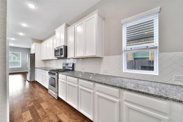 32193 Park Plains Dr, Conroe, TX 77385 - kitchen with appliances with stainless steel finishes, white cabinets, dark wood finished floors, tasteful backsplash, and light stone counters