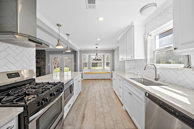 kitchen featuring visible vents, ornamental molding, a sink, appliances with stainless steel finishes, and wall chimney range hood