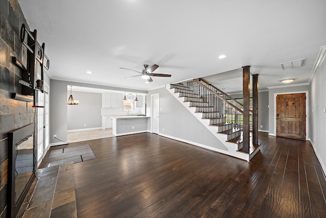 unfurnished living room with stairs, ornamental molding, a tile fireplace, wood finished floors, and a ceiling fan