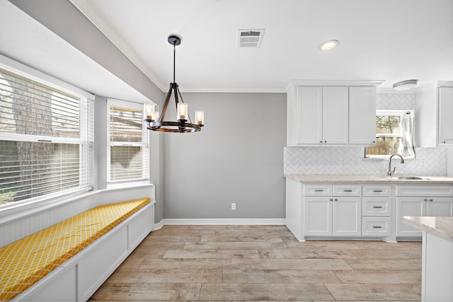 kitchen featuring ornamental molding, a sink, white cabinets, a notable chandelier, and tasteful backsplash