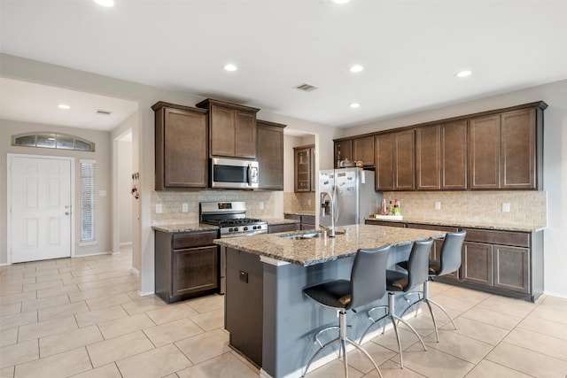 kitchen with visible vents, light stone counters, dark brown cabinetry, appliances with stainless steel finishes, and light tile patterned flooring