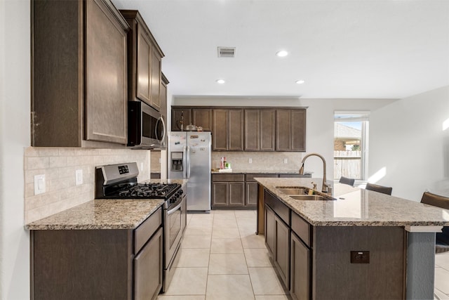 kitchen with visible vents, a kitchen island with sink, a sink, stainless steel appliances, and dark brown cabinets