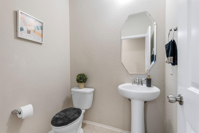 half bath featuring toilet, baseboards, and a sink