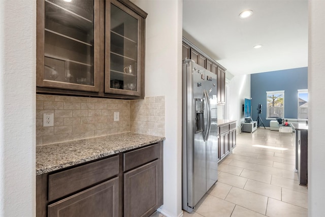 kitchen featuring dark brown cabinetry, backsplash, light stone countertops, and stainless steel fridge with ice dispenser