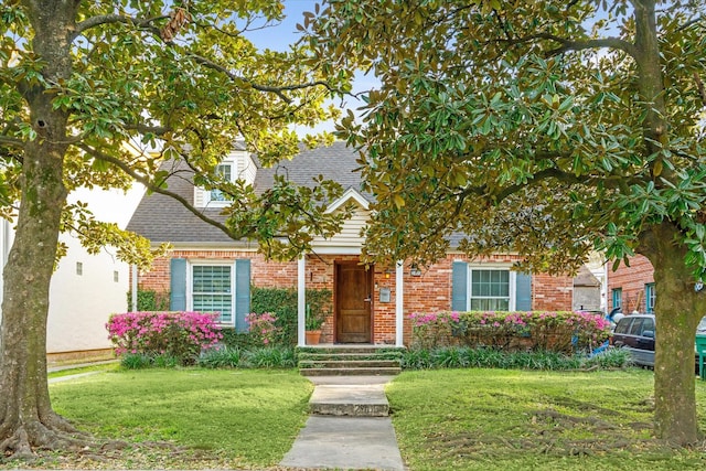 view of front of house with brick siding, a front yard, and a shingled roof