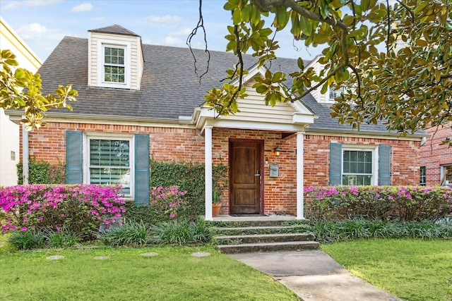 cape cod-style house with a front yard, brick siding, and a shingled roof