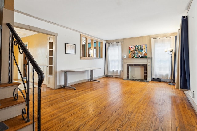 unfurnished living room with stairs, a tiled fireplace, baseboards, and wood-type flooring