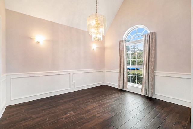 spare room with dark wood-style floors, lofted ceiling, a chandelier, and a wainscoted wall