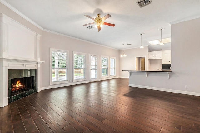 unfurnished living room featuring visible vents, ceiling fan with notable chandelier, dark wood finished floors, crown molding, and a fireplace