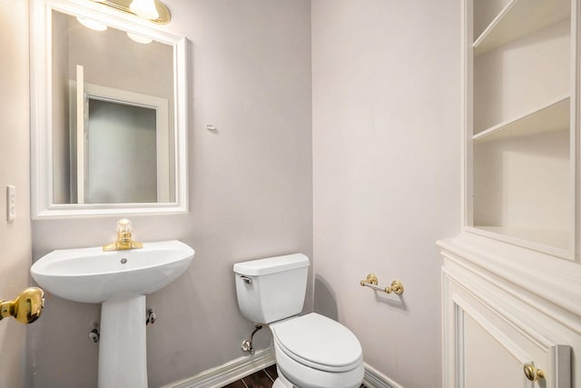 half bath featuring wood finished floors, toilet, baseboards, and a sink