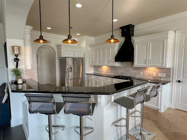 kitchen with custom range hood, dark countertops, stainless steel fridge, a peninsula, and decorative backsplash