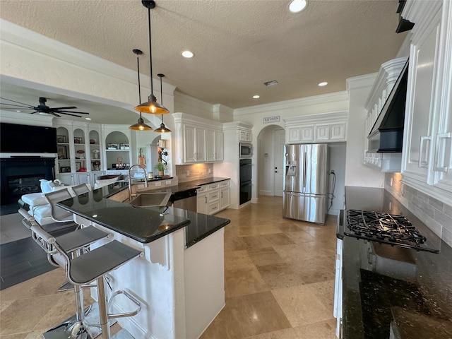 kitchen with arched walkways, a glass covered fireplace, stainless steel appliances, a ceiling fan, and a sink