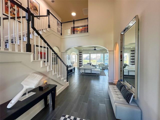 entrance foyer featuring a ceiling fan, wood finished floors, stairway, arched walkways, and a towering ceiling