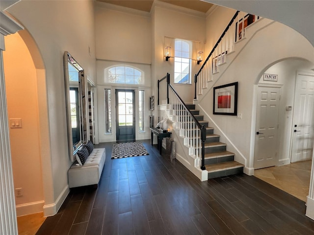 entryway with stairs, crown molding, arched walkways, and dark wood-style flooring