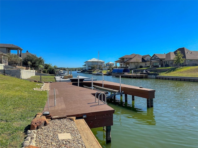 view of dock with a residential view, a water view, a yard, and fence