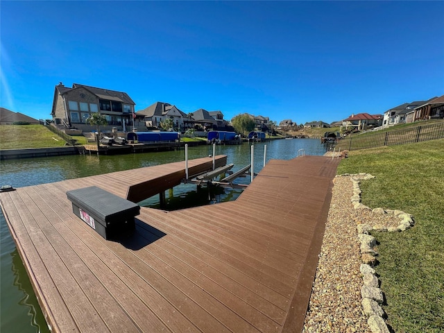 view of dock with a residential view, fence, a yard, and a water view