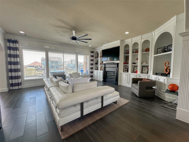 living area featuring a glass covered fireplace, a textured ceiling, a ceiling fan, and dark wood-style flooring