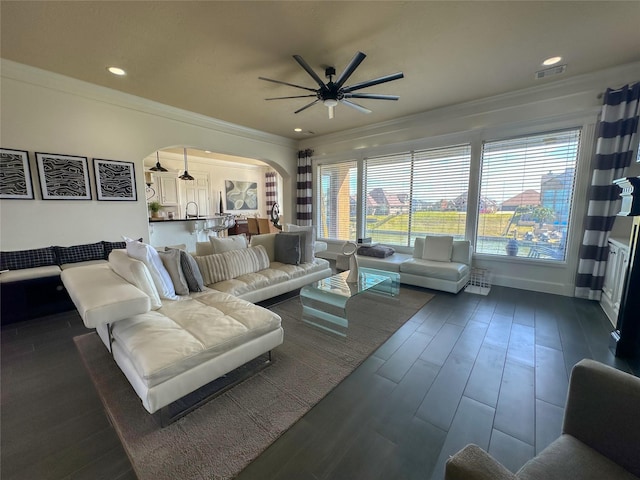 living room with visible vents, crown molding, arched walkways, a ceiling fan, and dark wood-style flooring