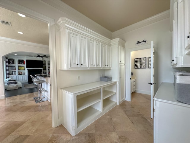 kitchen featuring a ceiling fan, visible vents, arched walkways, ornamental molding, and light countertops