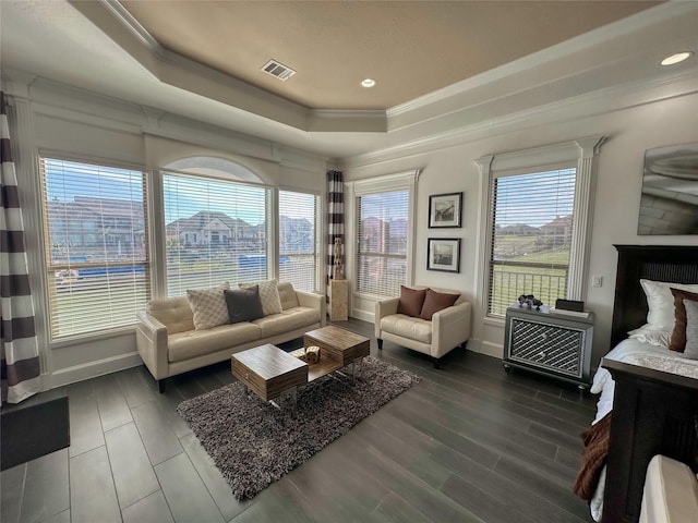 living room featuring wood finished floors, baseboards, visible vents, a tray ceiling, and ornamental molding