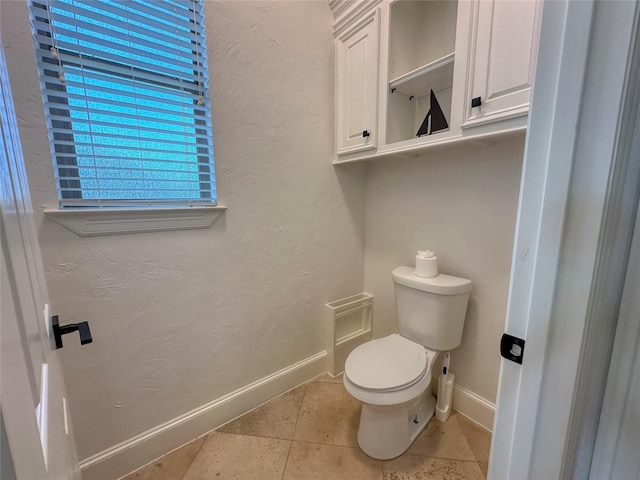 bathroom featuring tile patterned floors, toilet, a textured wall, and baseboards