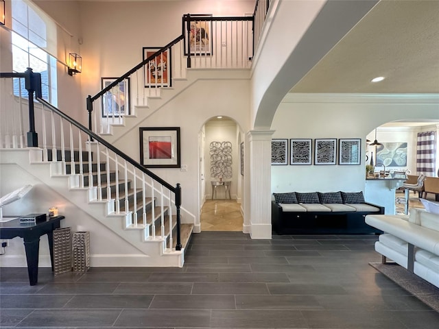 entrance foyer featuring baseboards, wood tiled floor, arched walkways, stairs, and a towering ceiling